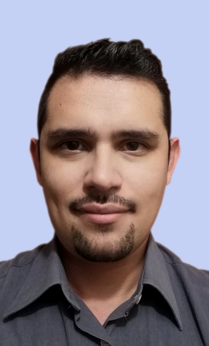 Joseph Gama wearing a gray collared shirt, standing against a light blue background, appearing neutral and professional